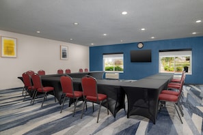 Een vergaderzaal met een lange tafel, rode stoelen, een klok en een raam met uitzicht.