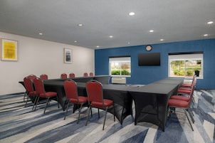 Un salón de conferencias con una larga mesa, sillas rojas, un reloj y una ventana con vistas.