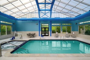 A swimming pool with a glass ceiling, surrounded by lounge chairs and a table. - Holiday Inn Express & Suites Southfield Detroit by IHG (Southfield)
