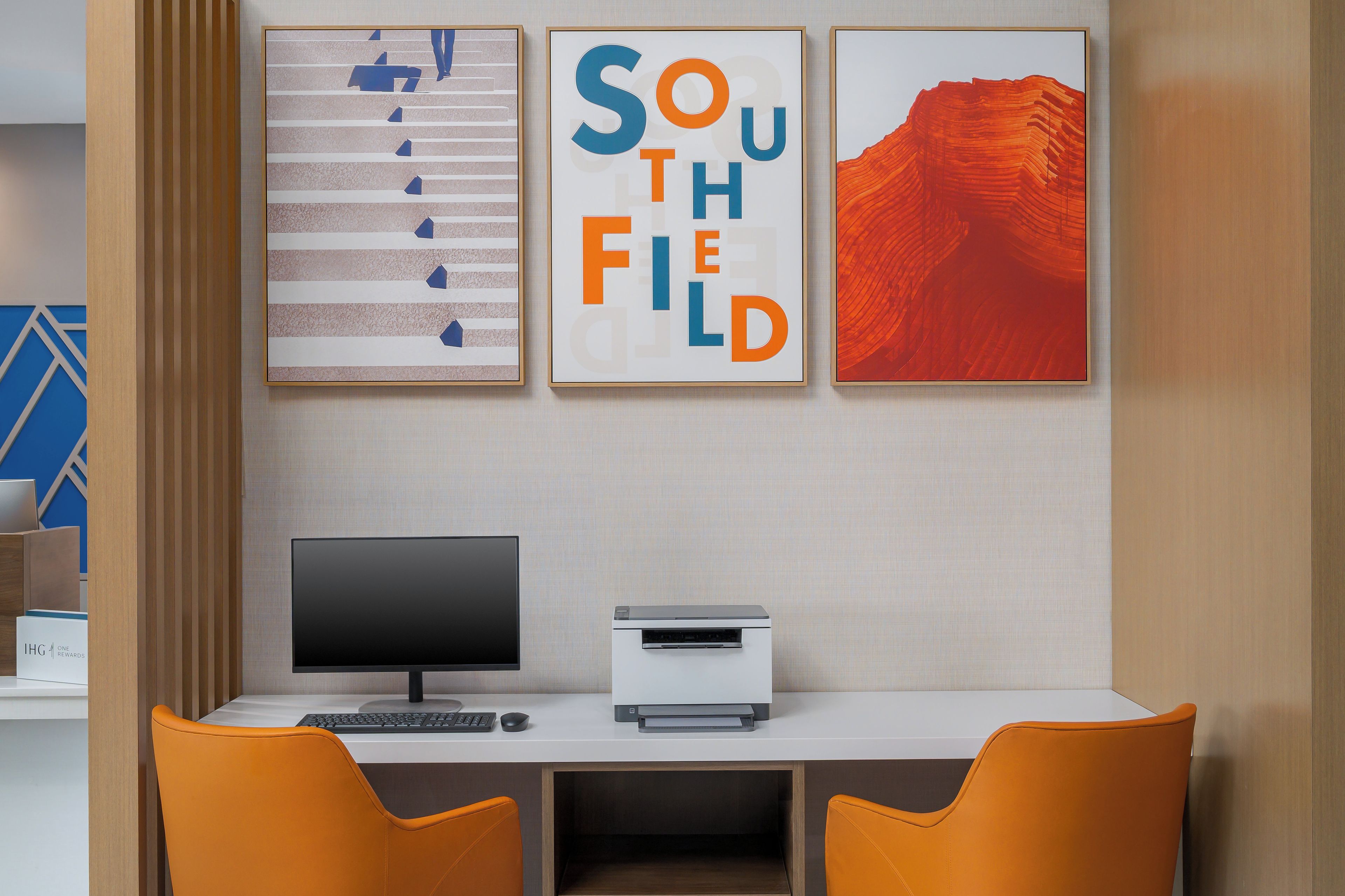 Ein modernes Büro mit Schreibtisch, zwei Stühlen, einem Computer und einem Drucker. An der Wand hängen drei gerahmte Kunstwerke.
