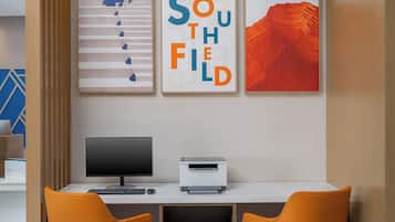 Ein modernes Büro mit Schreibtisch, zwei Stühlen, einem Computer und einem Drucker. An der Wand hängen drei gerahmte Kunstwerke.