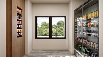 A hallway with a wooden shelf on the left, a large window with a view of trees, and a refrigerated beverage display on the right.