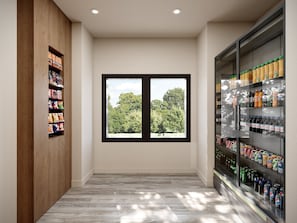 A hallway with a wooden shelf on the left, a large window with a view of trees, and a refrigerated beverage display on the right. - Holiday Inn Express & Suites Southfield Detroit by IHG (Southfield)