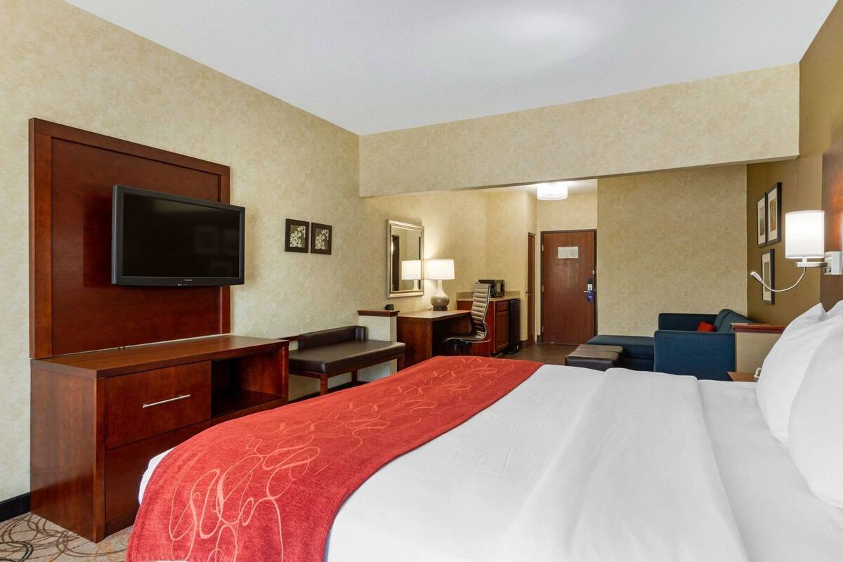Ein Hotelzimmer mit einem großen Bett, einem Schreibtisch, einem Stuhl, einem Fernseher und einem Spiegel.