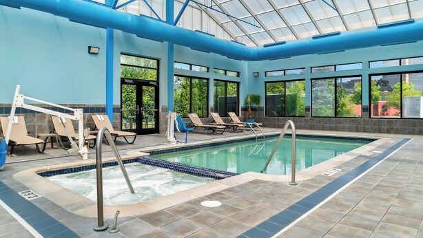 An indoor swimming pool with a glass ceiling, lounge chairs, and a view of the outside. - Holiday Inn Express & Suites Southfield Detroit by IHG (Southfield)