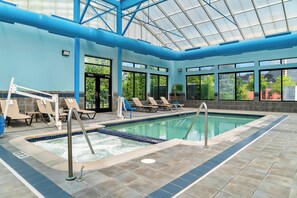 An indoor swimming pool with a glass ceiling, lounge chairs, and a view of the outside. - Holiday Inn Express & Suites Southfield Detroit by IHG (Southfield)