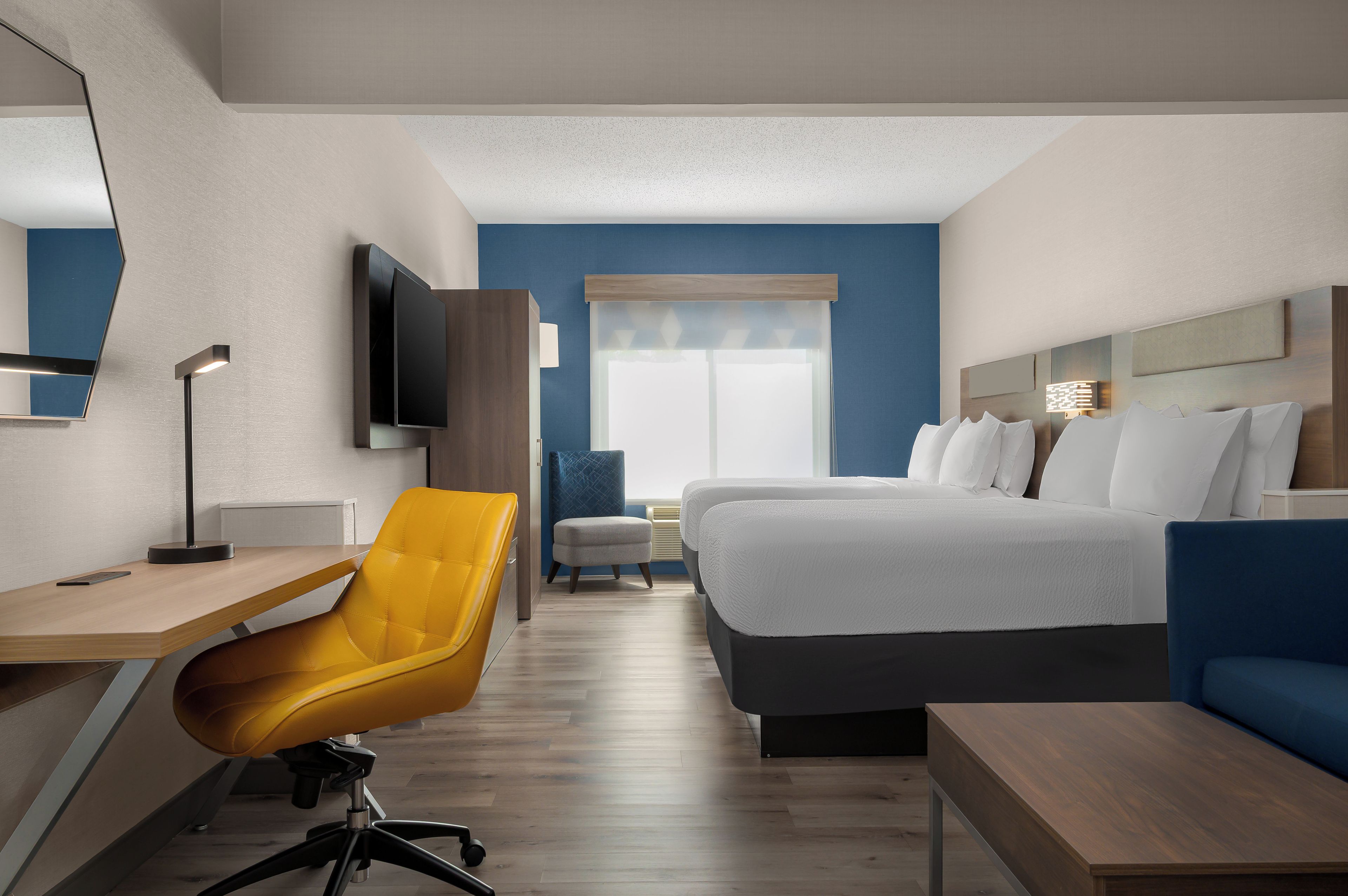 A hotel room with a bed, a desk, a chair, a TV, and a window.