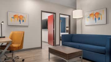 A modern living room with a blue sofa, a wooden coffee table, and a yellow office chair. There are two doors leading to other rooms, and artwork on the walls.