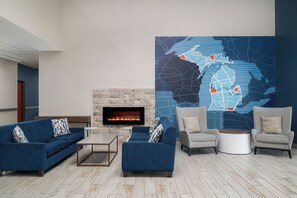 A modern lounge area with sofas, a fireplace, and a large abstract wall art piece. - Holiday Inn Express & Suites Southfield Detroit by IHG (Southfield)