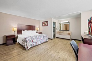 A hotel room with a bed, bedside tables, a desk, a chair, a mirror, and a bathroom door. - Red Roof Inn Abingdon (Abingdon)