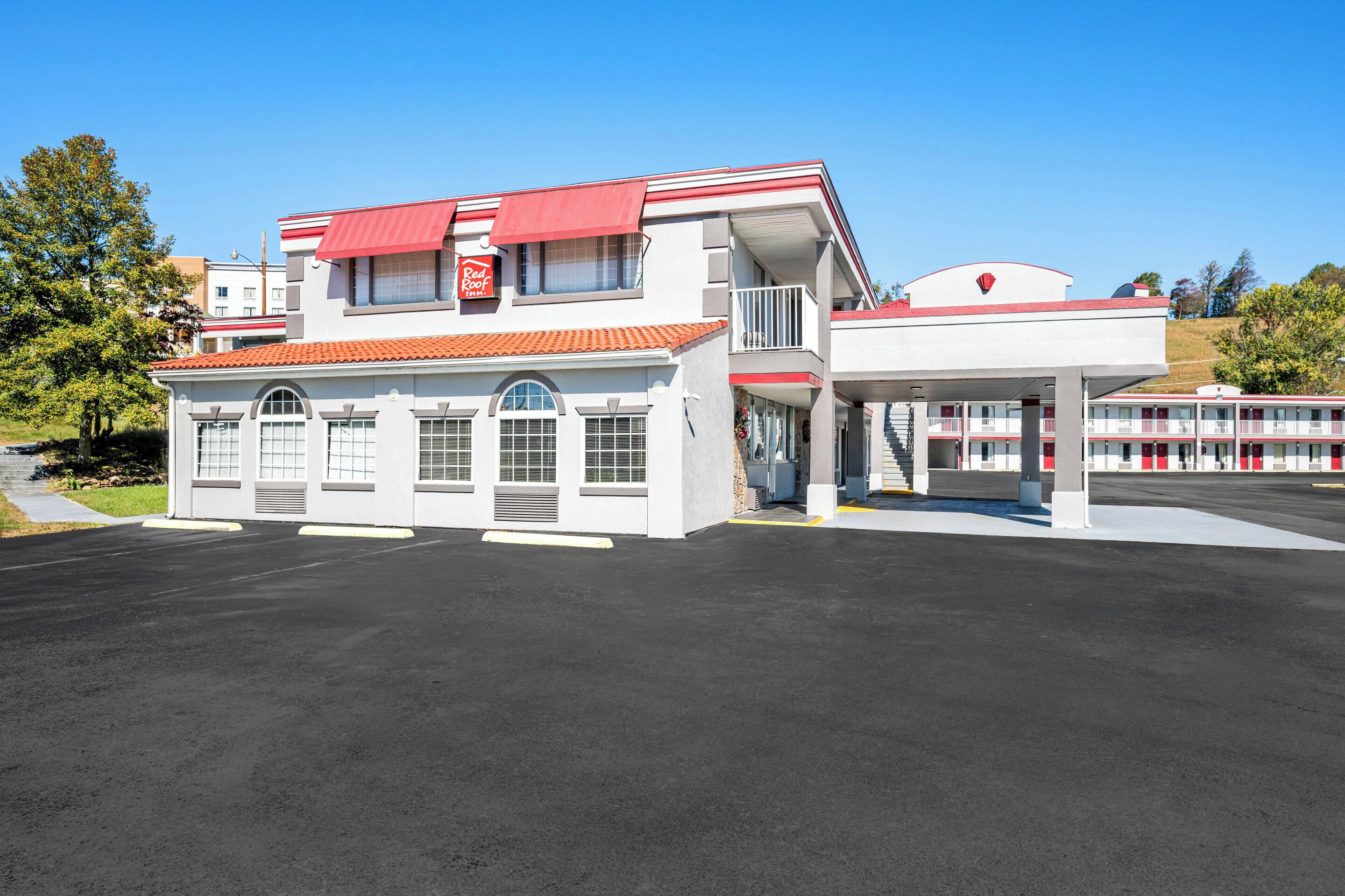 Un Red Roof Inn con un edificio de dos pisos, una zona de estacionamiento techada y un cielo azul despejado.