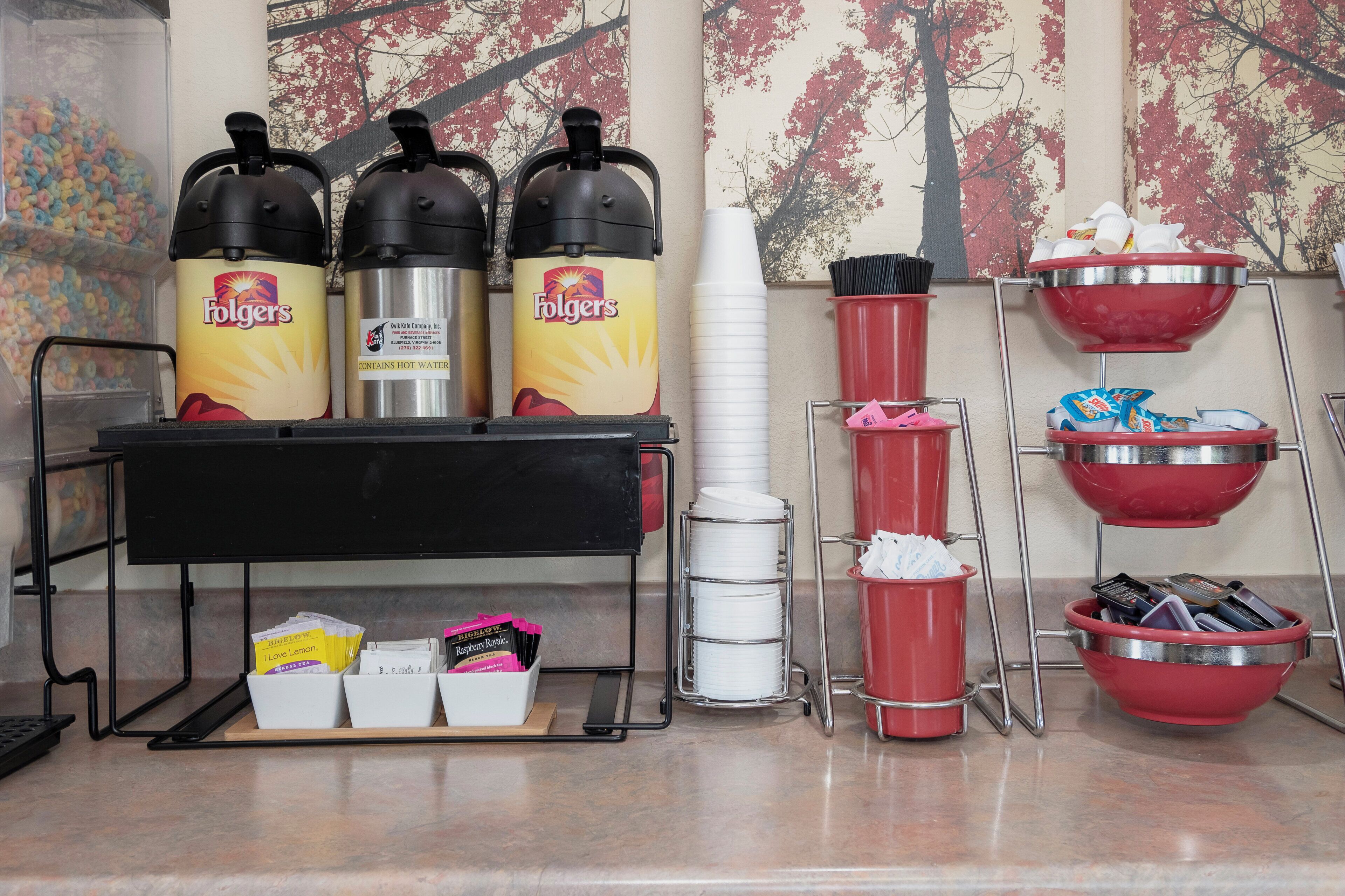 Un área de bebidas con dispensadores de agua caliente, una cafetera y un dispensador de té.