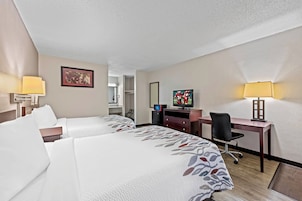 A hotel room with two beds, a desk, a TV, and a lamp.