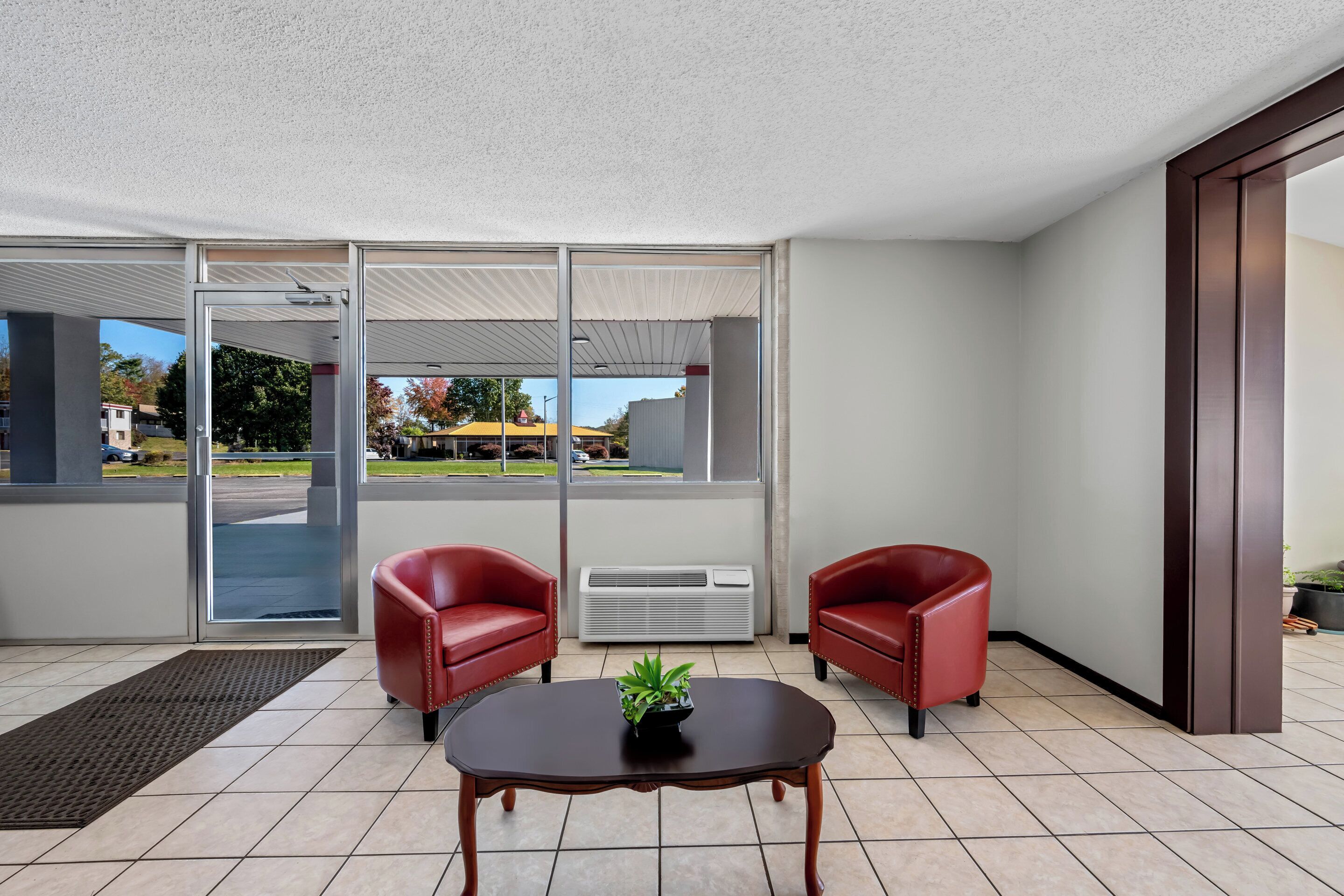 Una habitación moderna con dos sillones de cuero rojo, una mesa de madera con una planta y puertas de cristal grandes que dan a un estacionamiento.