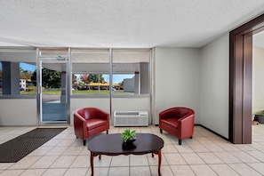 A modern room with two red leather chairs, a wooden table with a plant, and large glass doors leading to a parking area. - Red Roof Inn Abingdon (Abingdon)