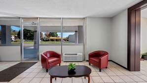 A modern room with two red leather chairs, a wooden table with a plant, and large glass doors leading to a parking area. - Red Roof Inn Abingdon (Abingdon)