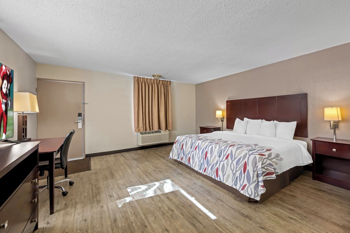 A hotel room with a large bed, a desk with a chair, a TV, and a window with curtains.