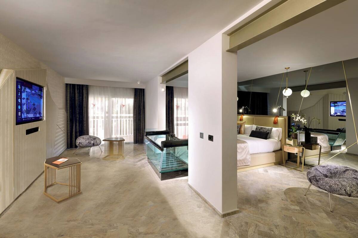 Ein modernes Hotelzimmer mit einem großen Bett, einem Schreibtisch, einem verglasten Balkon und einem Fernseher.