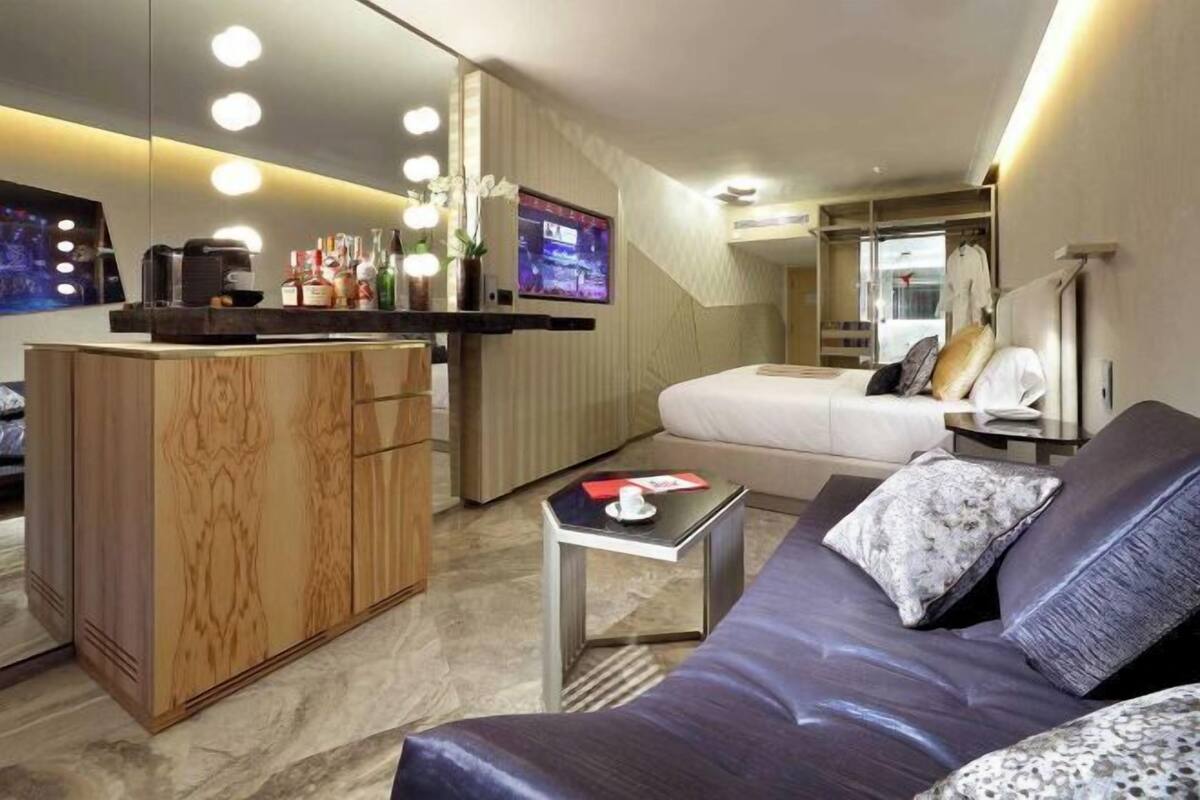 Ein modernes Hotelzimmer mit einem Holzkasten, einem Flachbildfernseher, einem Bett, einer Couch und einem kleinen Tisch.