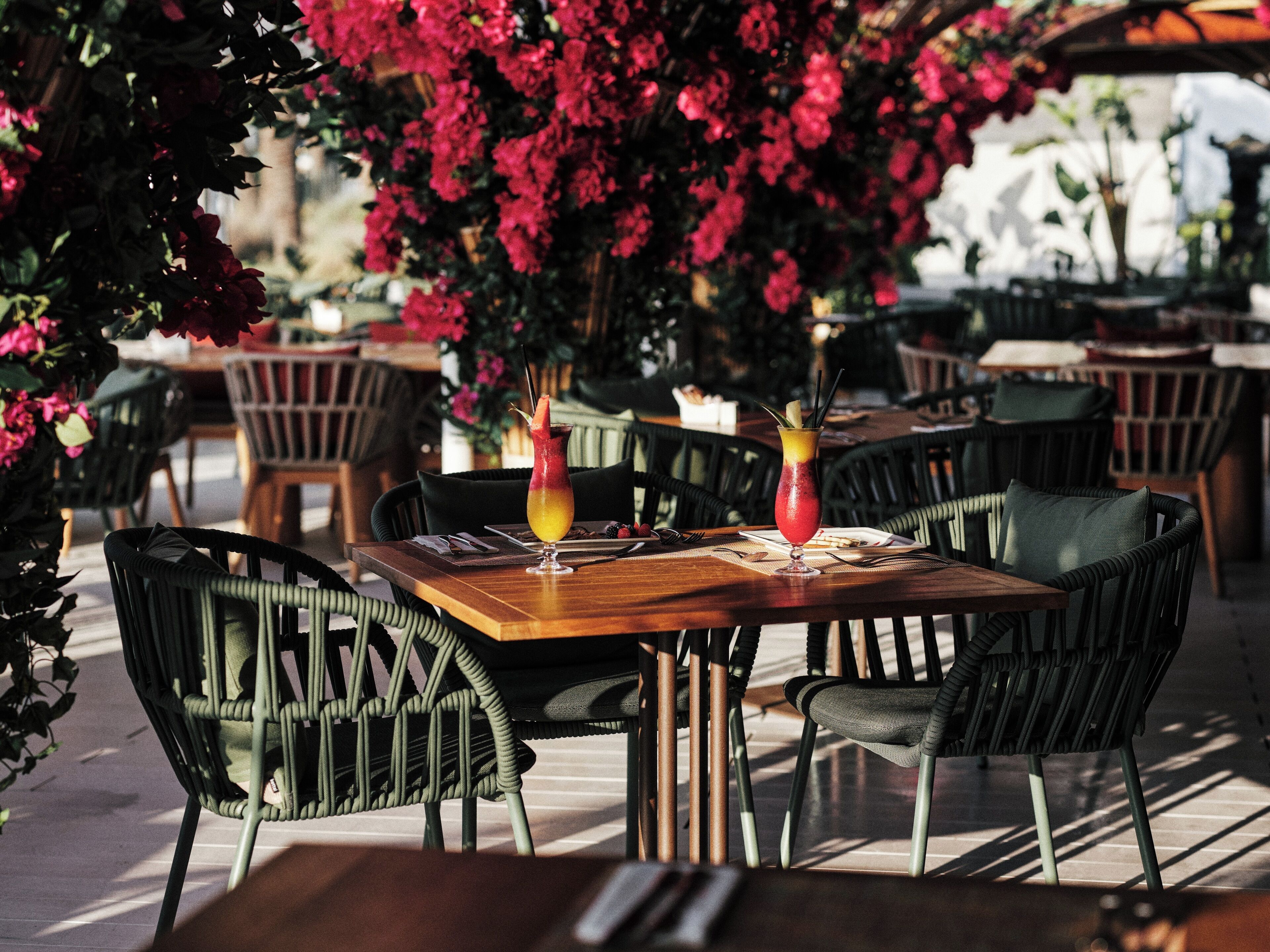 Ein Restaurant mit Außenbereich, Holztischen und grünen Stühlen.