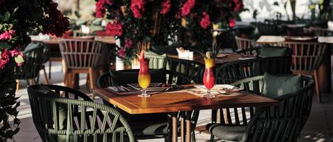 A restaurant with outdoor seating, wooden tables, and green chairs.