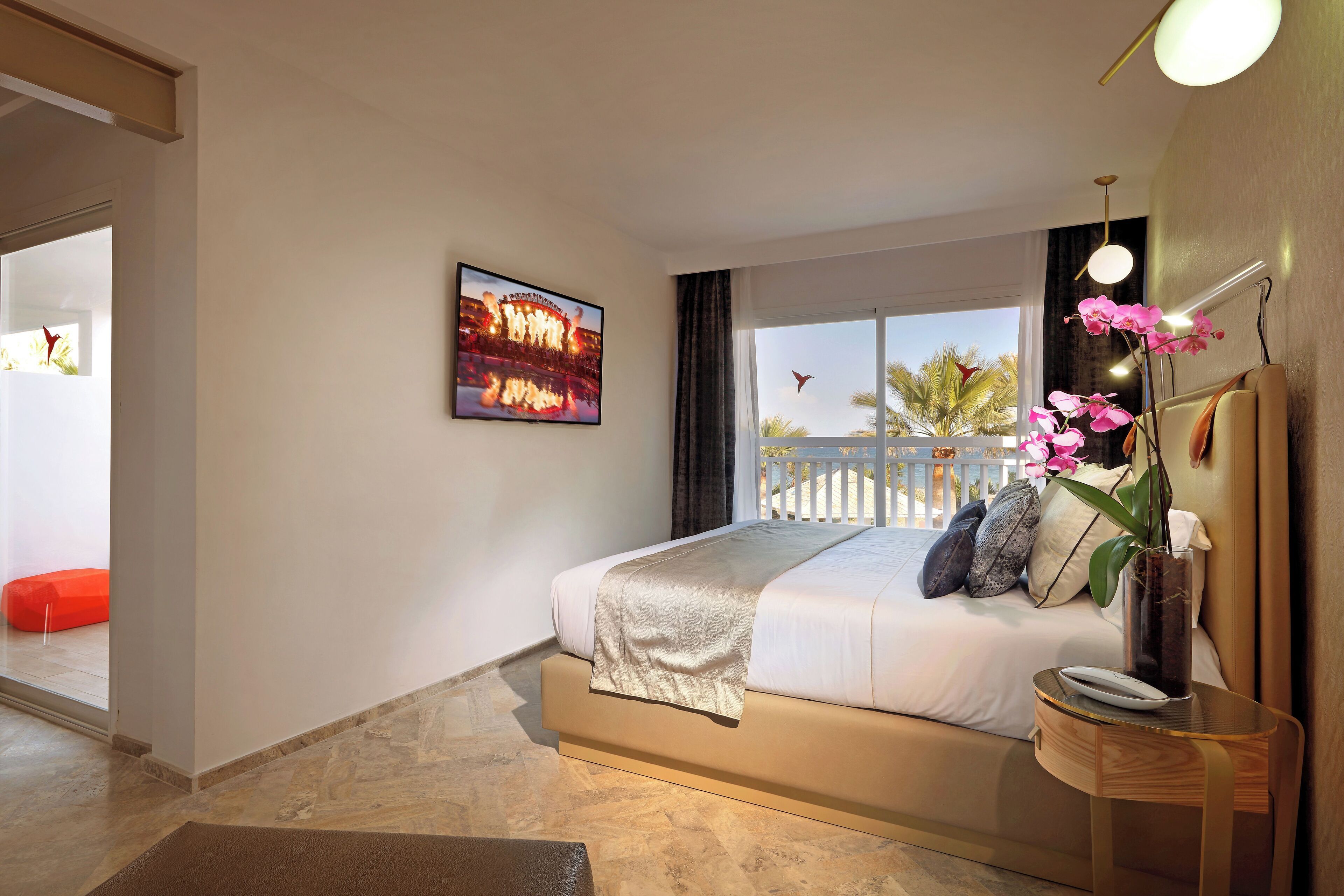 Ein modernes Hotelzimmer mit einem großen Bett, Meerblick, einem gerahmten Bild an der Wand und einem kleinen Tisch mit Blumen.