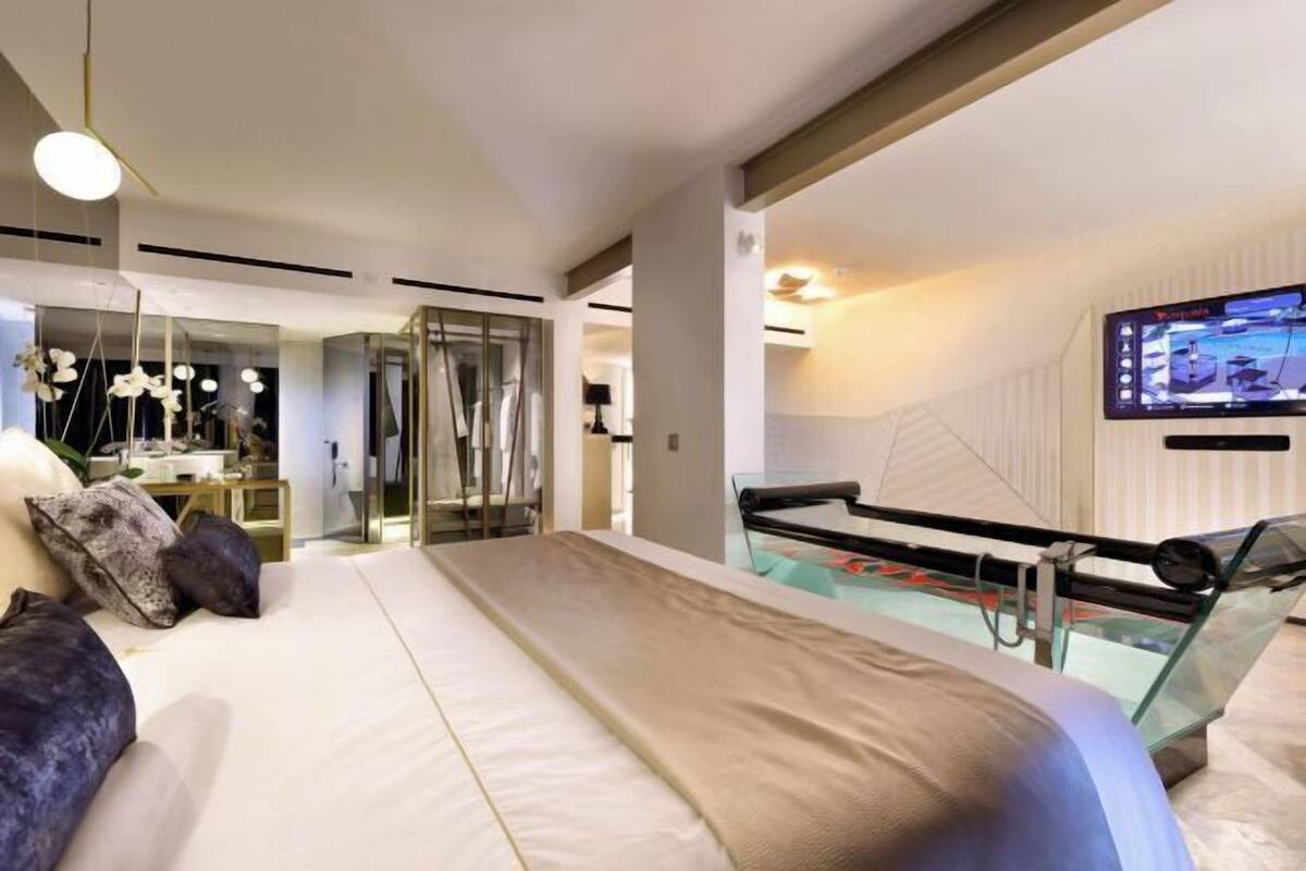 Ein modernes Schlafzimmer mit einem großen Bett, einem Glastisch und einem Fernseher an der Wand.