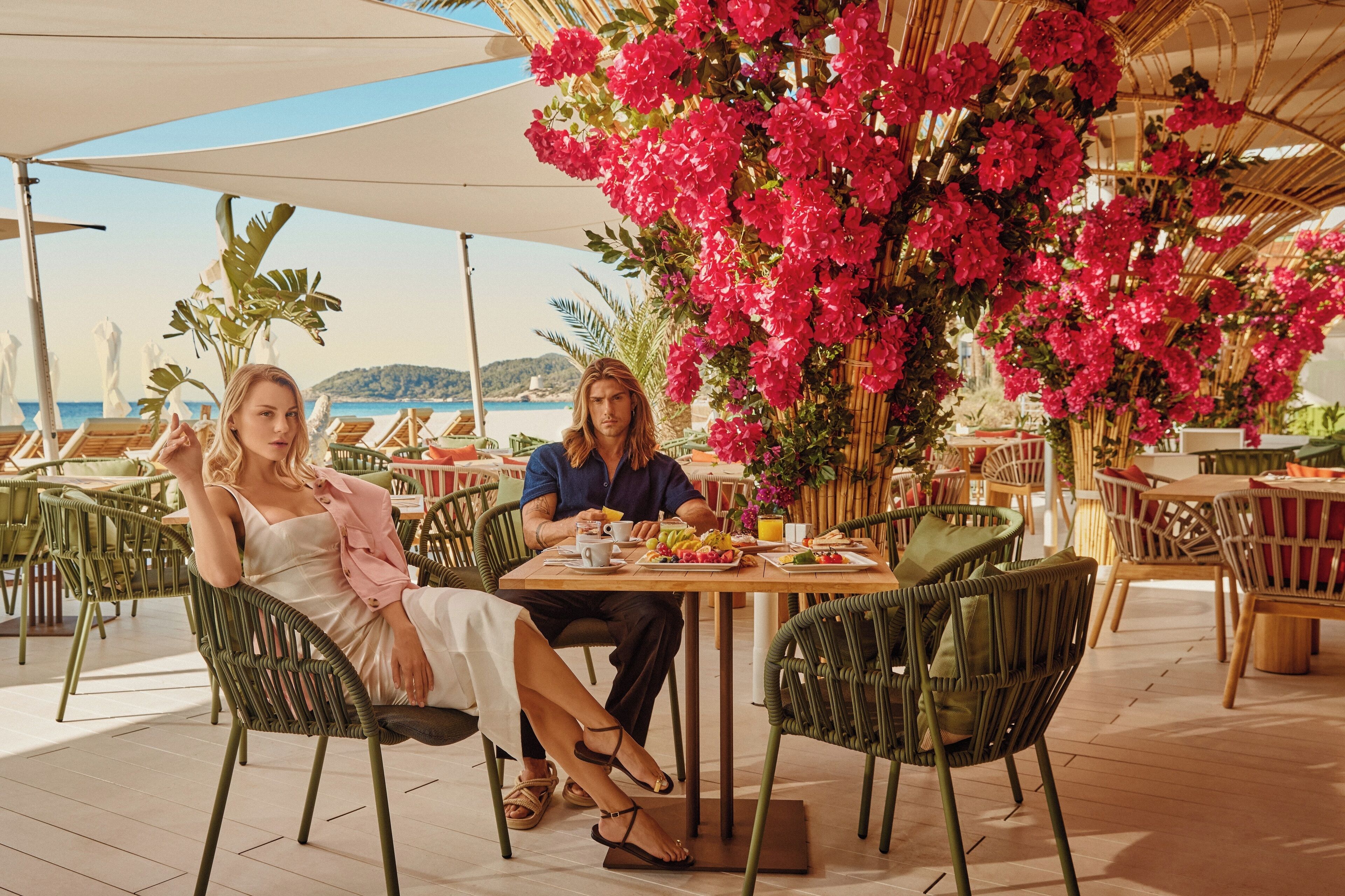 Un espace repas avec des sièges en plein air, des tables, des chaises et un décor composé de fleurs roses.