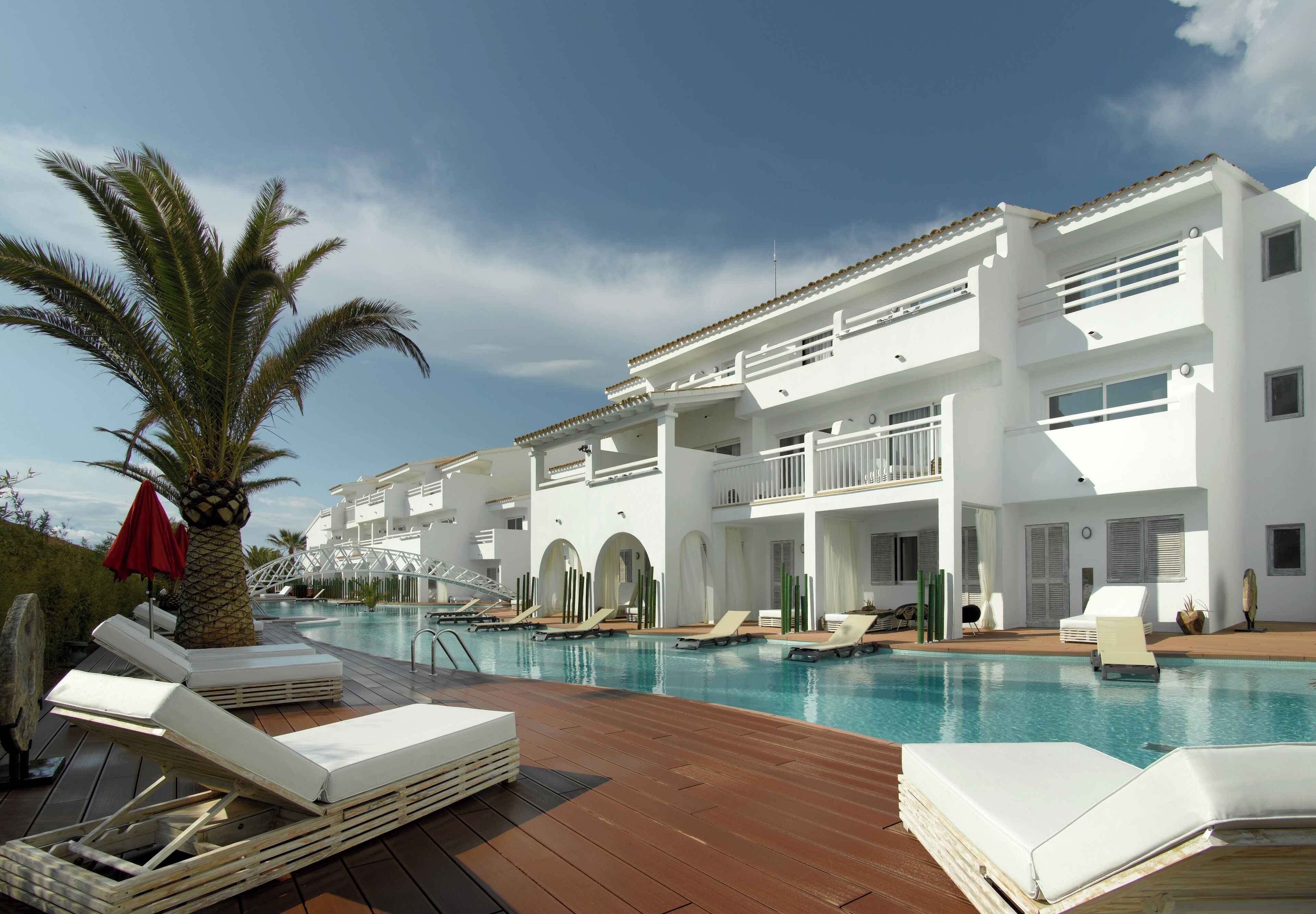 A modern hotel with a pool area, including lounge chairs and a palm tree.