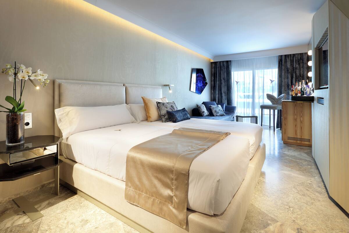 Ein modernes Hotelzimmer mit einem großen Bett, Nachttischen, einem Schminktisch mit Spiegel und einer Sitzecke mit Sessel und Tisch.