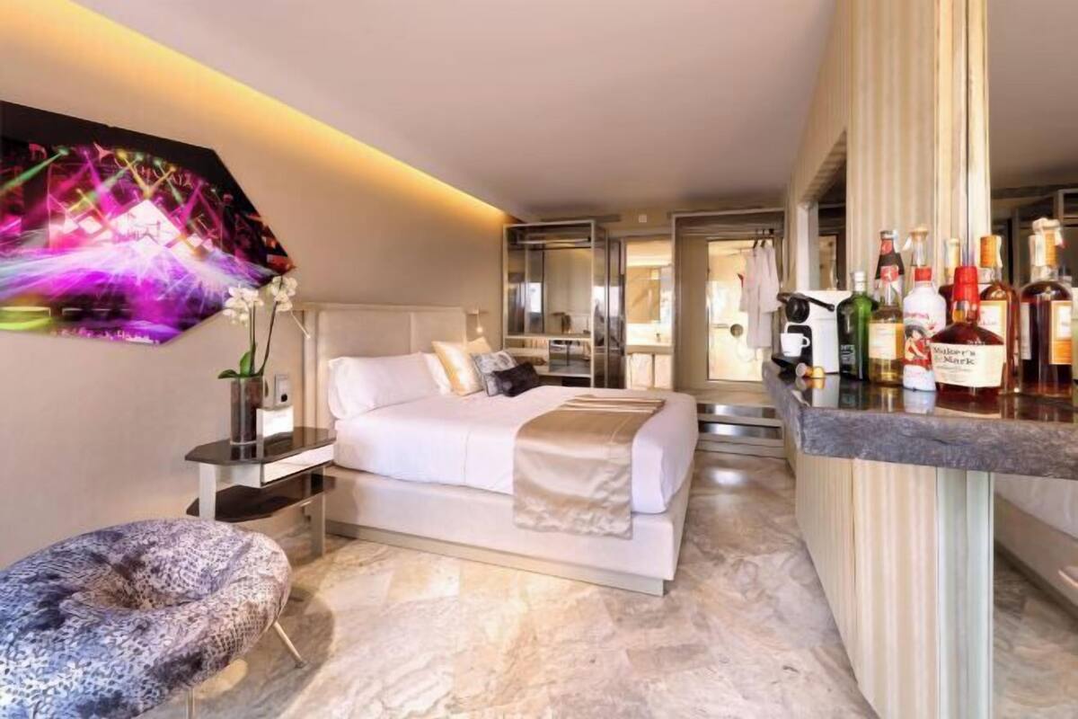 Ein modernes Hotelzimmer mit einem Bett, einer Sitzecke, einer Bar und einem großen Spiegel.