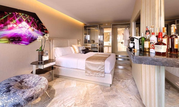 Una habitación de hotel moderna con cama, zona de estar, minibar y vistas al baño.
