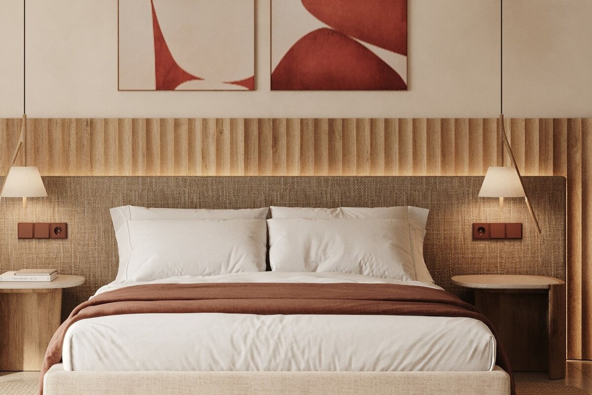 A hotel room with a large bed, two bedside tables, and a textured headboard.