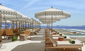 Un área de lounge en la azotea con sillones solárium, sombrillas y una piscina.