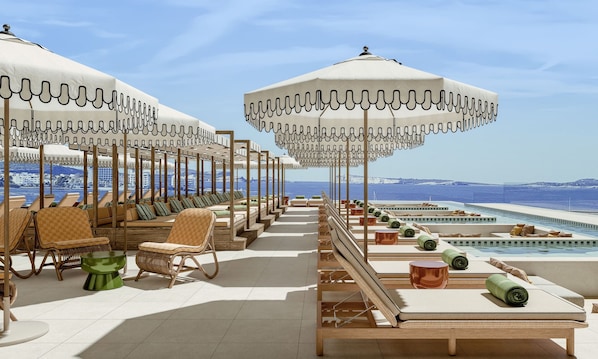 A rooftop lounge area with sun loungers, umbrellas, and a pool.
