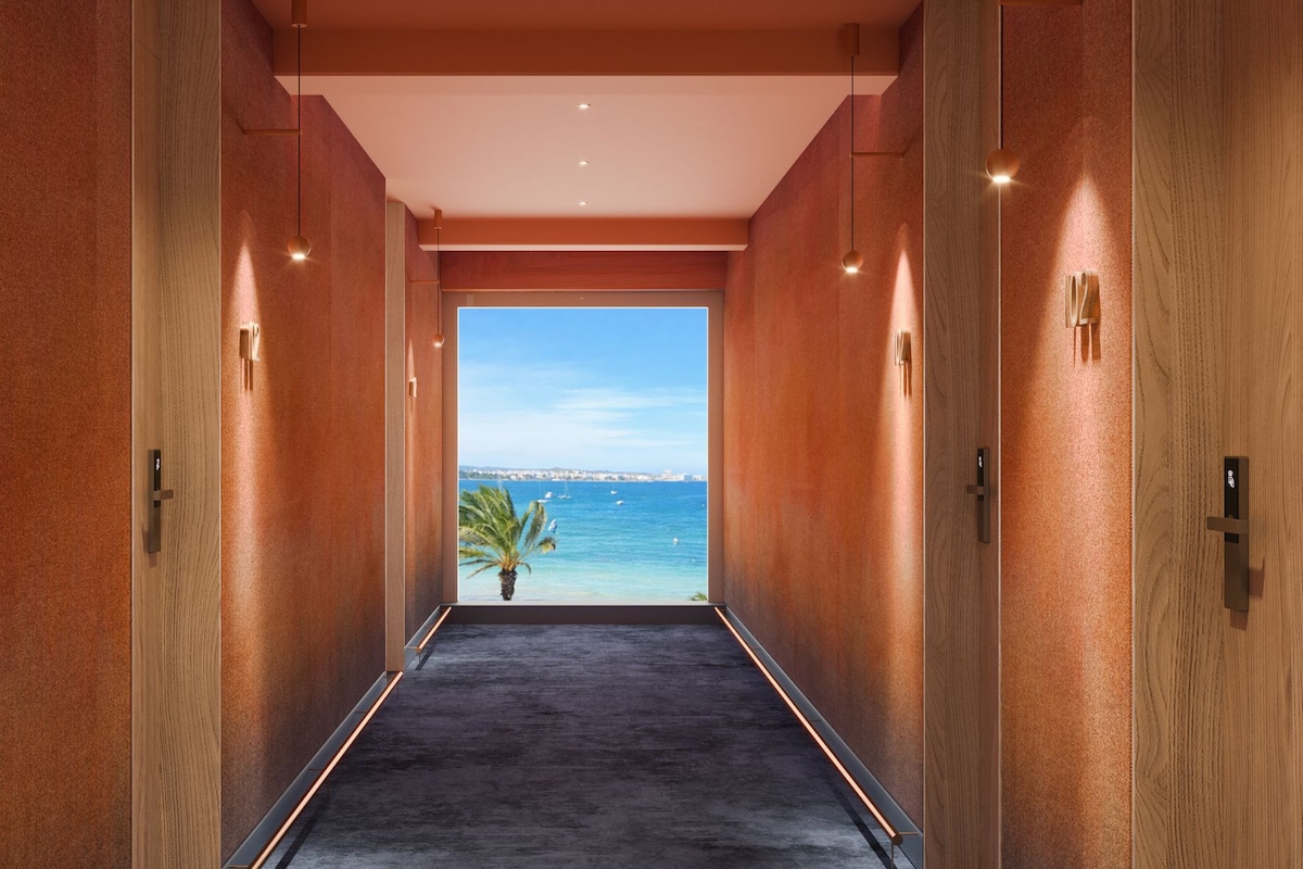 A hallway with a view of the sea, a palm tree, and a cityscape in the distance.