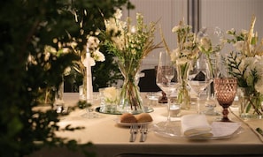 Una mesa dispuesta con vajilla transparente, flores blancas y una vela, que sugiere un ambiente de cena formal.