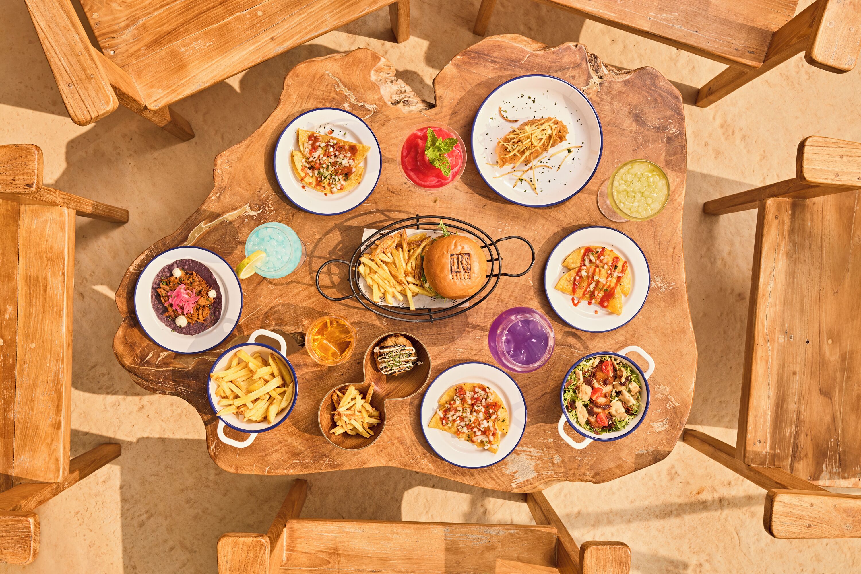 A wooden table with various dishes including a burger, fries, and salads.