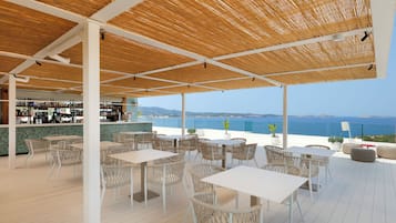 Un bar en la azotea con mesas blancas y sillas de mimbre, con vistas a la costa.