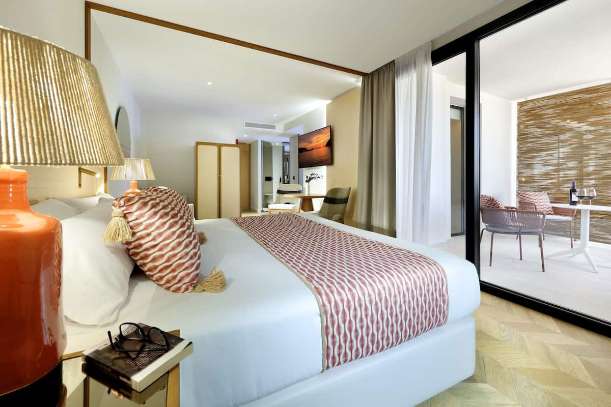A modern hotel room with a large bed, a desk, a chair, and a view of the outdoor area.
