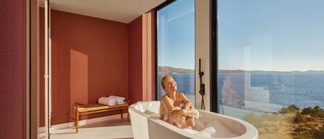 Une salle de bain moderne avec une grande baignoire, un banc et une vue sur la mer.