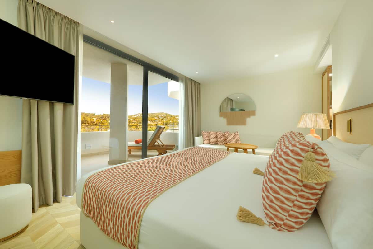 A hotel room with a large bed, a TV, a balcony with a view, and a small table.