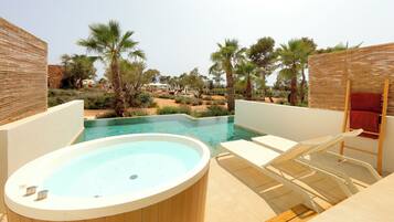 A hot tub and lounge chairs by a pool with palm trees and a view of the resort.