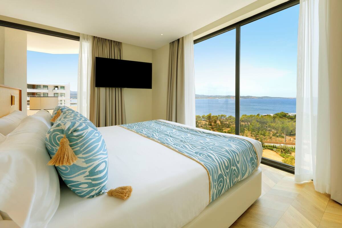 A modern hotel room with a large bed, a flat-screen TV, and a view of the sea.