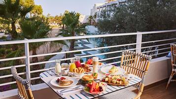 Un balcon avec une table préparée pour le petit-déjeuner, comprenant des assiettes de nourriture, un verre de jus de fruits et une bouteille de lait.