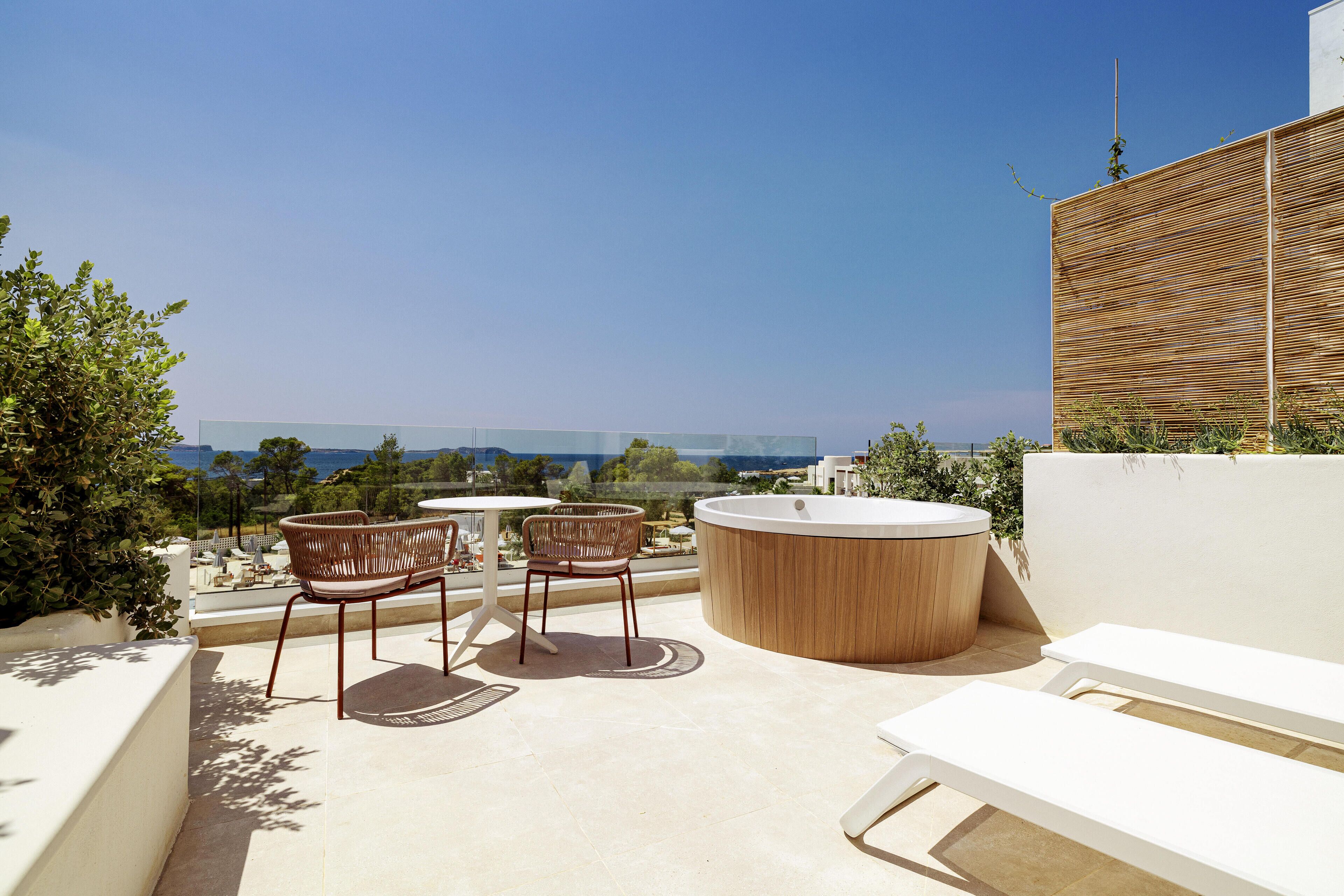 A rooftop terrace with a hot tub, two wicker chairs, and a lounge chair.