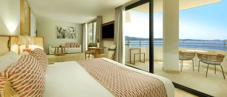 Une chambre d’hôtel moderne dotée d’un grand lit, d’une télévision, d’un balcon avec coin salon extérieur et d’une vue sur la mer.