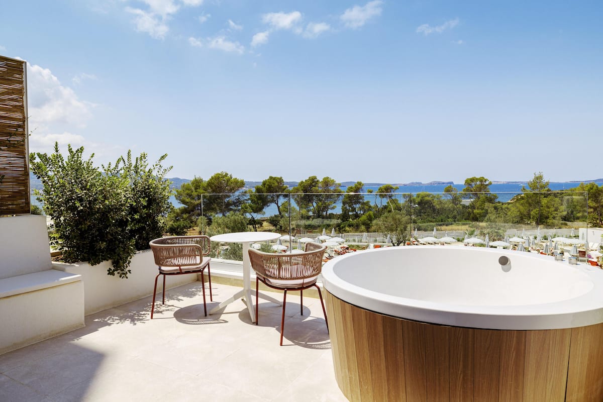 A rooftop terrace with a wooden bathtub, two wicker chairs, and a small round table.