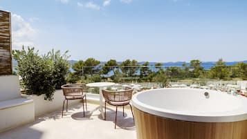 A rooftop terrace with a wooden bathtub, two wicker chairs, and a small round table.