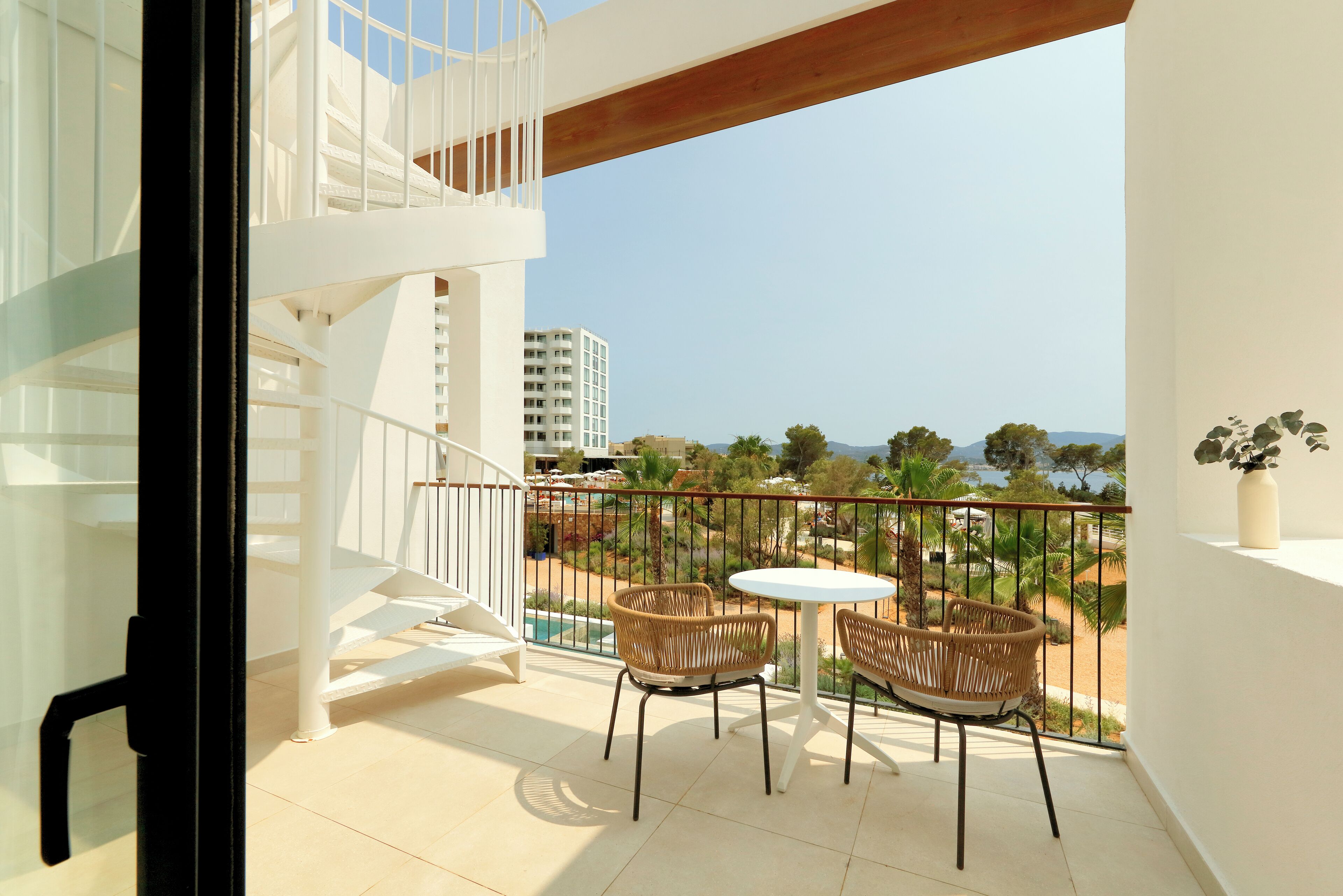 A balcony with a white railing, two wicker chairs, and a small table.